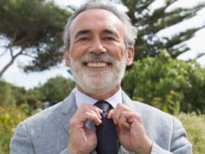 well-dressed man adjusting his tie and smiling confidently because of his high-quality dentures